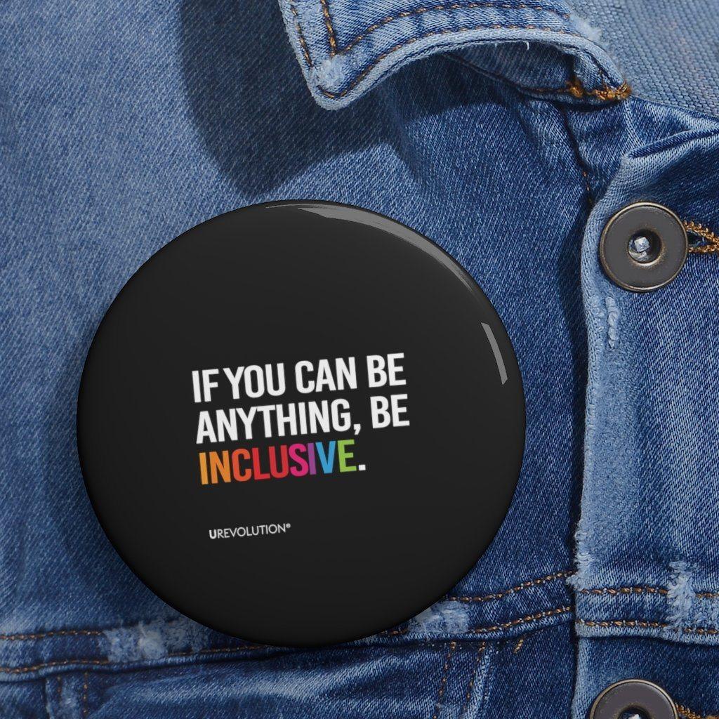 A Be Inclusive pin button. The phrase, "if you can be anything, be inclusive," is printed in upper white case letters against a black background. The word inclusive is in the colors of the rainbow.