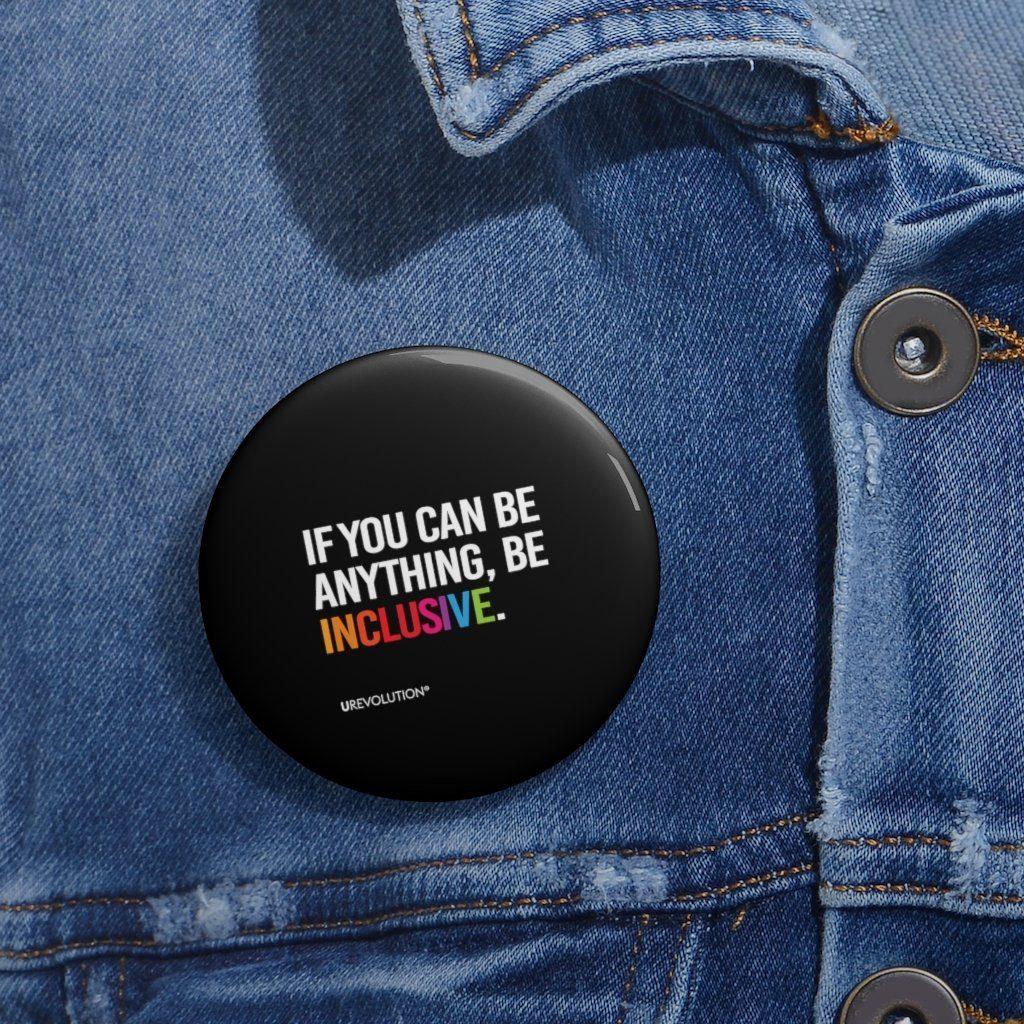 A Be Inclusive pin button. The phrase, "if you can be anything, be inclusive," is printed in upper white case letters against a black background. The word inclusive is in the colors of the rainbow.
