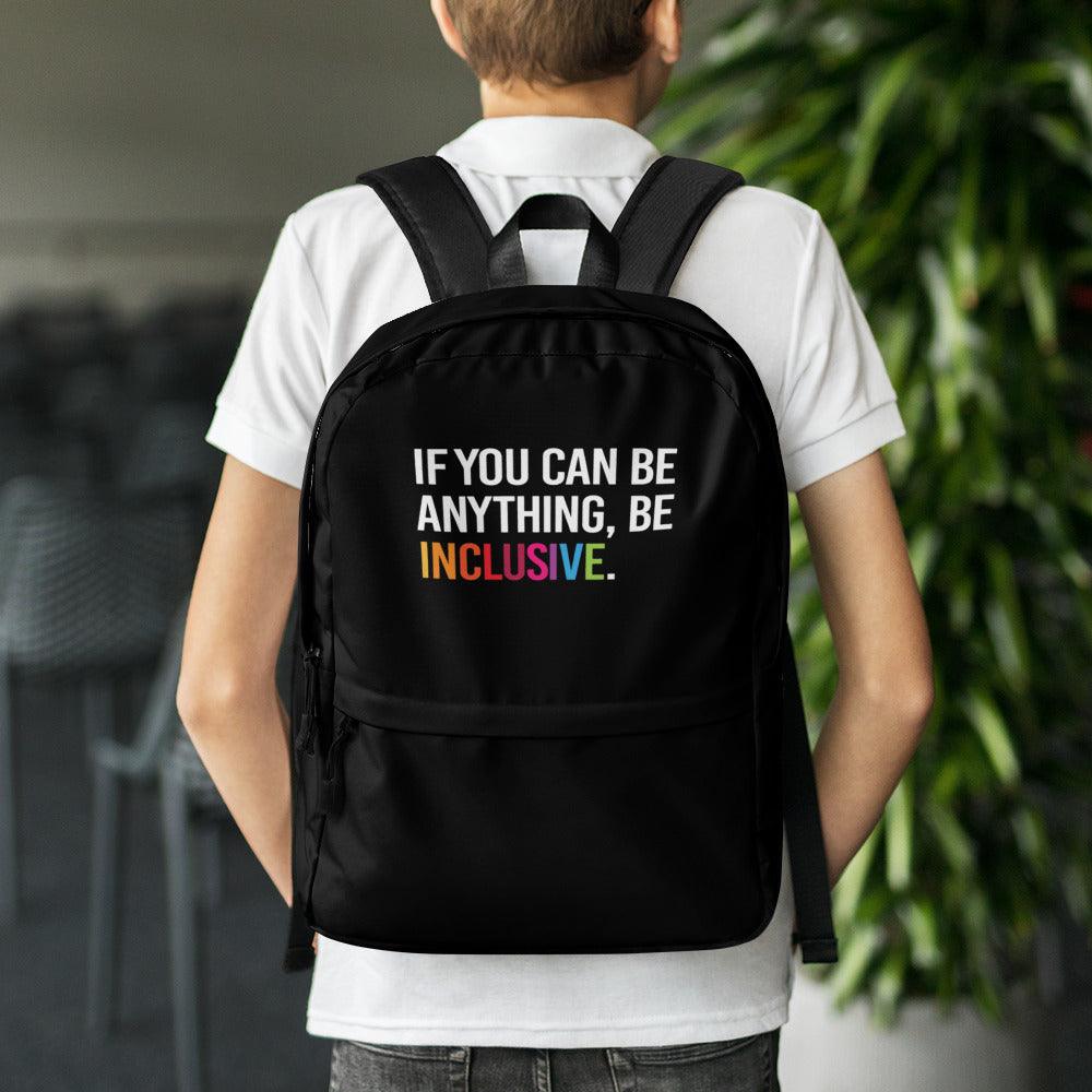 This is a photo of URevolution's black Be Inclusive backpack. In the top of half of the backpack, the phrase, 'If you can be anything, be inclusive,' is printed in white upper case letters. The rest of the backpack is black. The word 'inclusive' is in the color of the rainbow.  The backpack is work by a teenager wearing a white polo shirt and black jeans. 