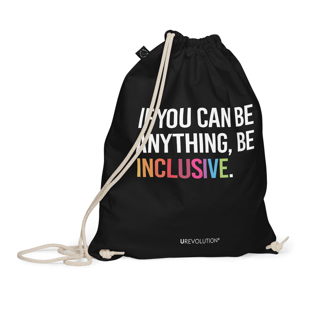 This is a photo of URevolution's black Be Inclusive organic cotton drawstring bag. In the middle of the drawstring bag, printed in large white upper case letters, is the phrase, 'If you can be anything, be inclusive.' The word 'inclusive' is in the color of the rainbow. At the bottom edge of the bag is the word, URevolution, printed in small white upper case letters. The bag's cotton drawstrings are pulling the top of the bag closed.