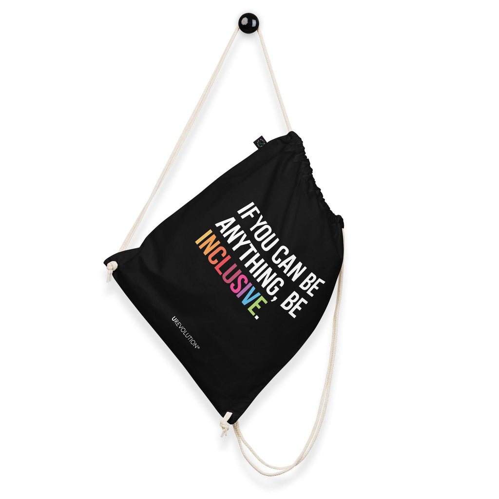 This is a photo of URevolution's black Be Inclusive organic cotton drawstring bag. In the middle of the drawstring bag, printed in large white upper case letters, is the phrase, 'If you can be anything, be inclusive.' The word 'inclusive' is in the color of the rainbow. At the bottom edge of the bag is the word, URevolution, printed in small white upper case letters. The bag's cotton drawstrings are pulling the top of the bag closed. The bag is hanging a wall hook.