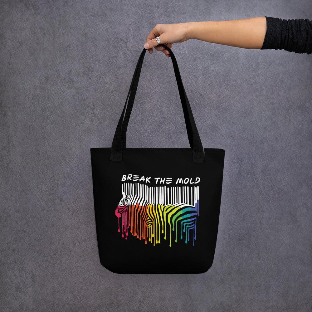 An image of a black tote bag against a plain background. In the middle of the bag is a graphic of zebra in the silhouette of a barcode. The top half of the zebra are vertical white stripes, which then change just below the back into the colours of the rainbow. The bottom of each stripe has a paint drip mark. Just above the zebra's back is the phrase, in upper case, 'break the mold.'