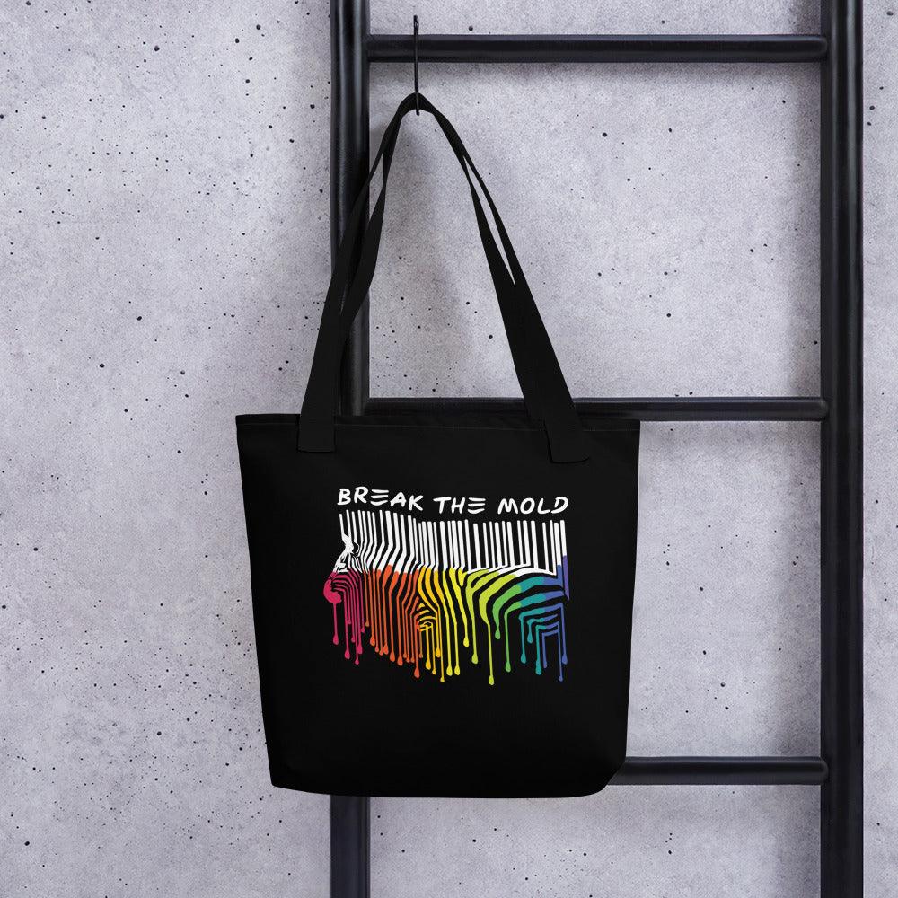 An image of a black tote bag against a plain background. In the middle of the bag is a graphic of zebra in the silhouette of a barcode. The top half of the zebra are vertical white stripes, which then change just below the back into the colours of the rainbow. The bottom of each stripe has a paint drip mark. Just above the zebra's back is the phrase, in upper case, 'break the mold.'