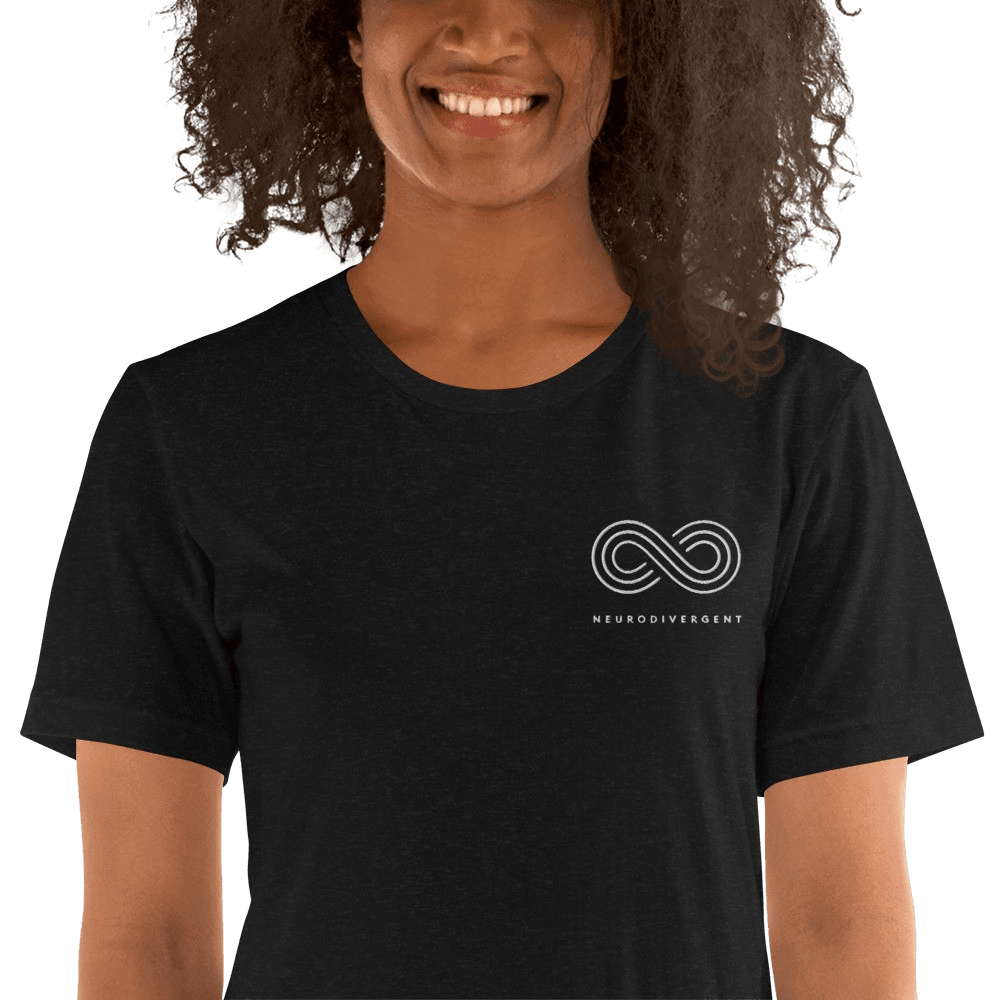 This is a photo of a black heather embroidered Neurodivergent Tee. In the top left third of the Neurodivergent Hoodie, there is an elegant white infinity symbol consisting of three interwoven white lines. Under the symbol is the word, 'neurodivergent.' The neurodivergent t-shirt is worn by a black model. Only their torso is visible.