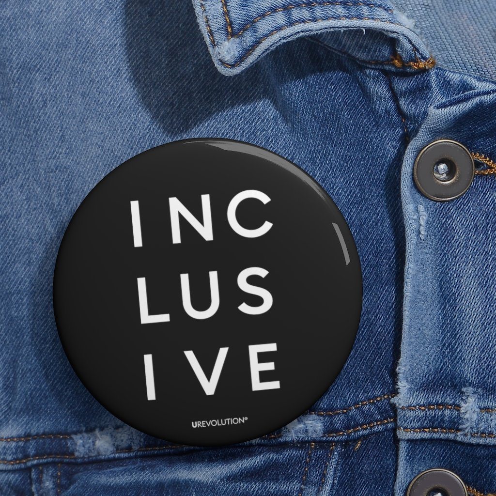 3" black inclusive pin button. On the front of the inclusive pin button is the word inclusive. The word inclusive is printed in black over three lines, with three letters on each line: INC LUS IVE. On the bottom edge of the pin, beneath the word inclusive, is the word URevolution in a small discrete font. horizontal black line. The pin is positioned on the left-hand side of a blue denim jacket beneath the lapel.