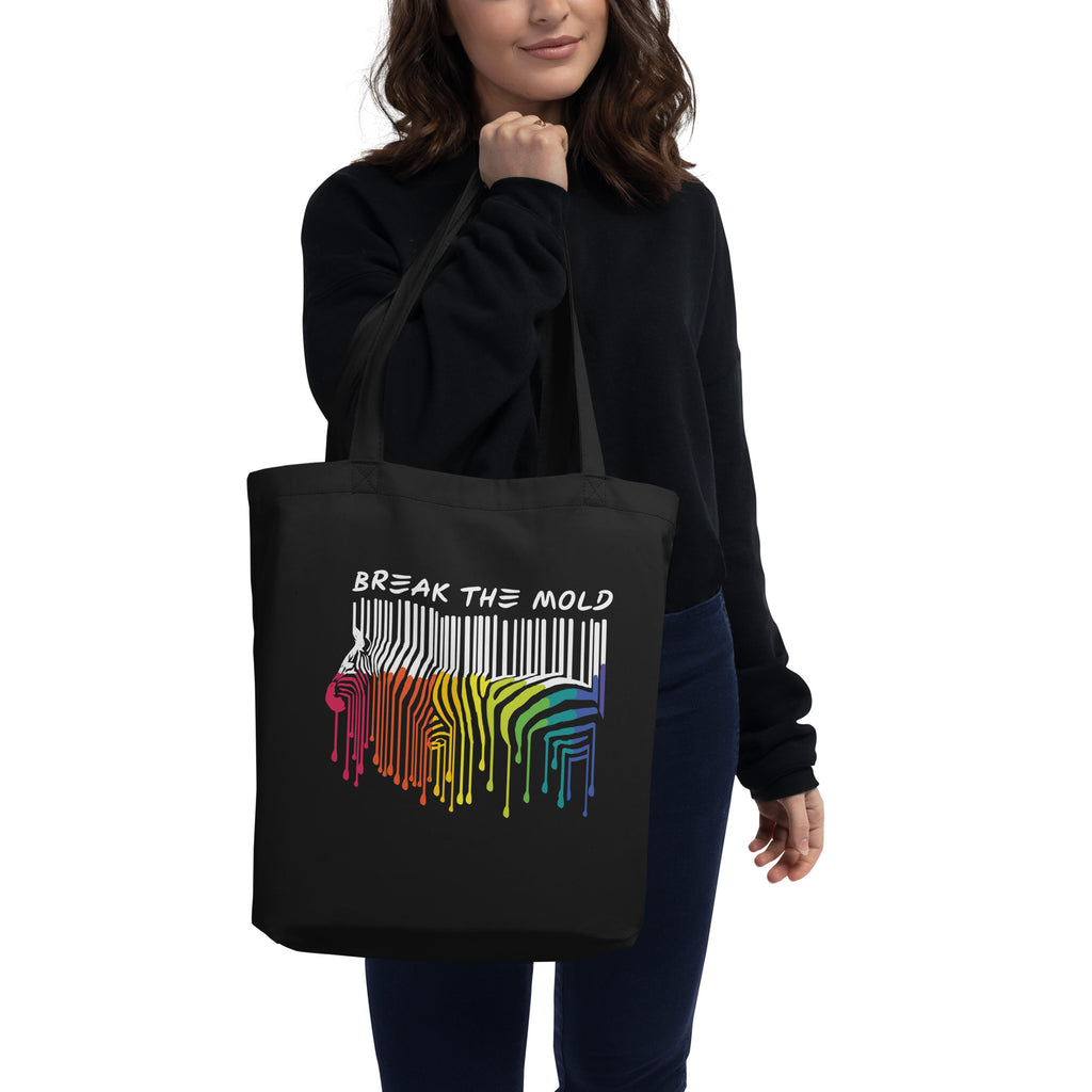 A photo of a black organic break the mold tote bag. In the middle of the break the mold tote is a graphic of zebra in the silhouette of a barcode. The top half of the zebra are vertical black stripes, which then change just below the back into the colors of the rainbow. The bottom of each stripe has a paint drip mark. Just above the zebra's back is the phrase, in upper case, 'break the mold.'