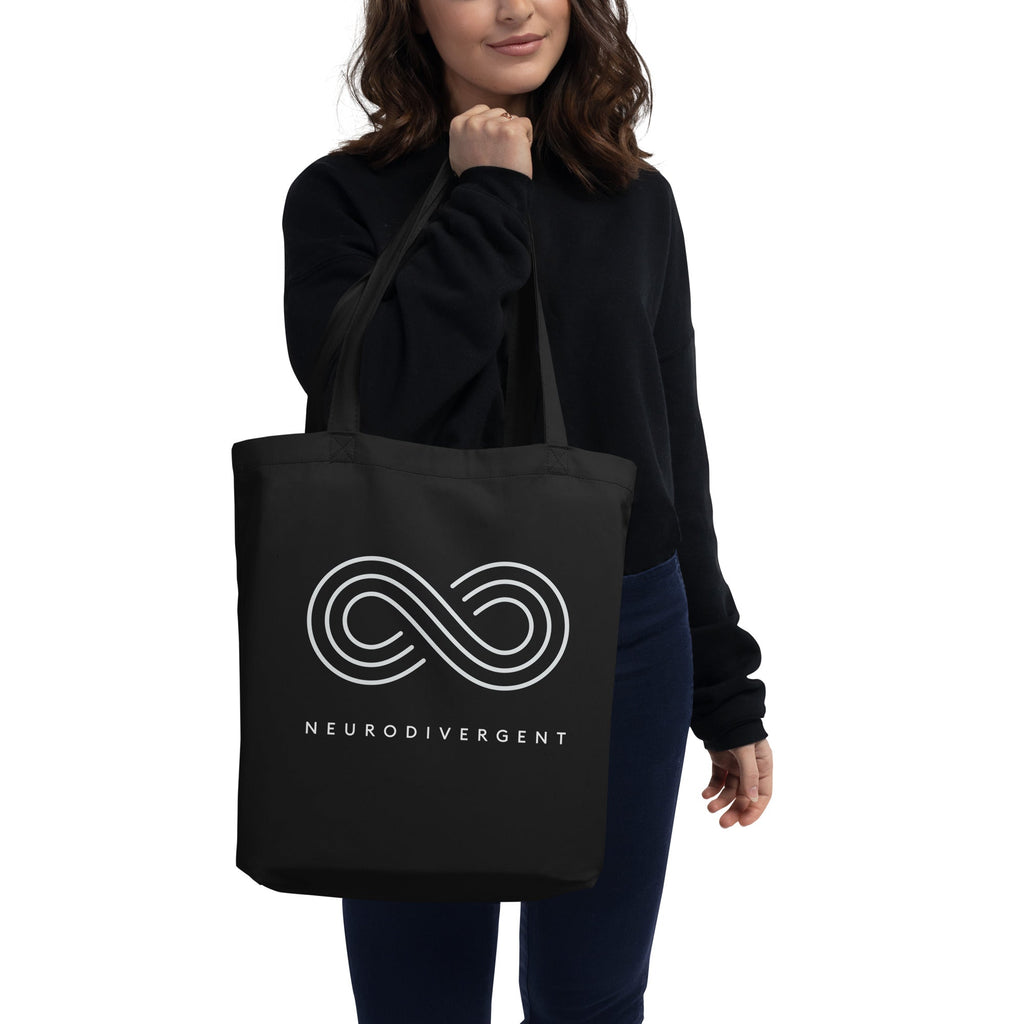 This is a photo of a black organic neurodivergent tote bag. In the middle of the tote is an elegant white infinity symbol consisting of three thin white lines. Just below the infinity symbol is the word Neurodivergent in elegant upper case white letters.