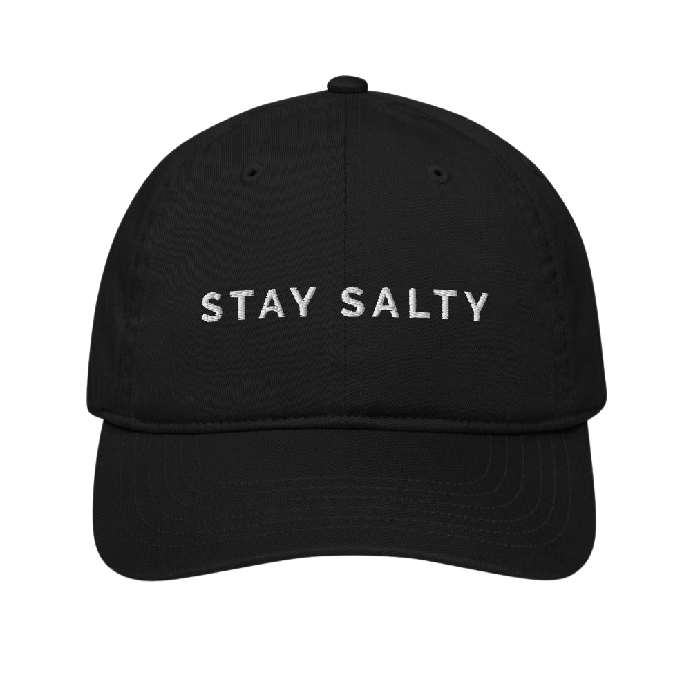 A photo of a black organic Stay Salty cap lying flat against a plain background. On the front panel of the cap the phrase, 'Stay Salty,' is embroidered on it in white upper case letters.