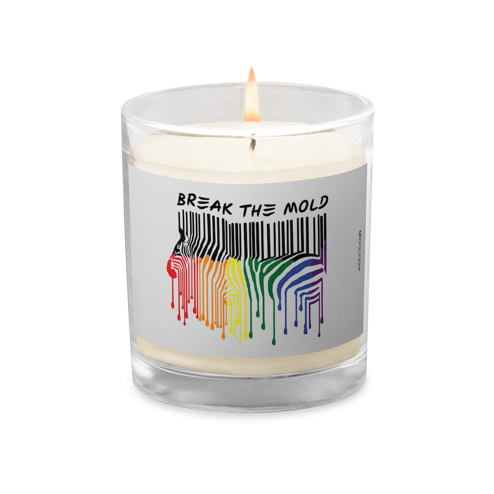 Break The Mold soy wax candle. In the middle of the candle is a zebra graphic in the silhouette of a barcode. The top half of the zebra are vertical black stripes, which change just below the back into the colors of the rainbow. The bottom of each strip has a paint drip mark. Above the zebra's back is the phrase, in upper case, 'break the mold.'  The candle's wick is burning.