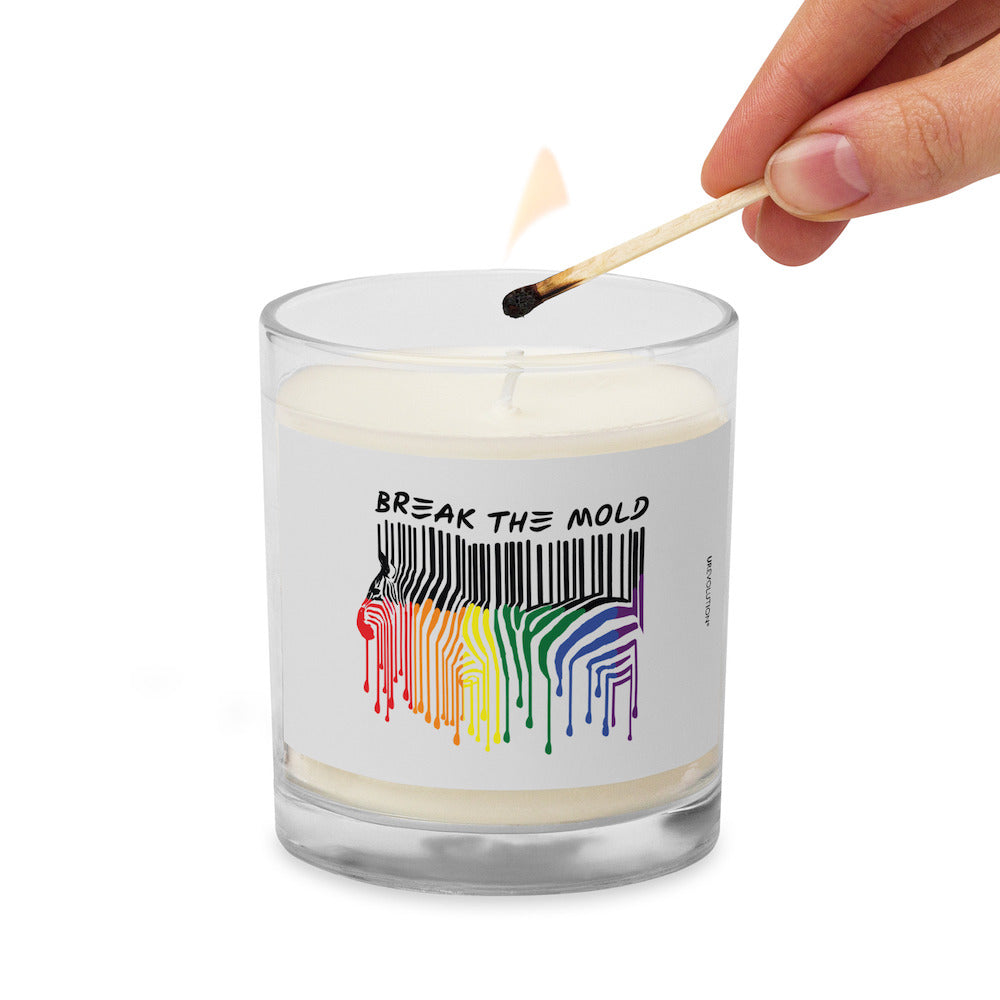 Break The Mold soy wax candle. In the middle of the candle is a zebra graphic in the silhouette of a barcode. The top half of the zebra are vertical black stripes, which change just below the back into the colors of the rainbow. The bottom of each strip has a paint drip mark. Above the zebra's back is the phrase, in upper case, 'break the mold.' The candle's cotton wick is being lit.