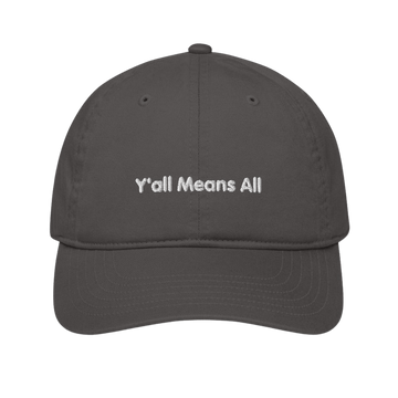 This is a photo of a charcoal-colored organic Y'all Means All cap lying flat against a plain background. On the front panel of the cap the phrase, 'Y'all Means All,' is embroidered on it in white upper case letters.