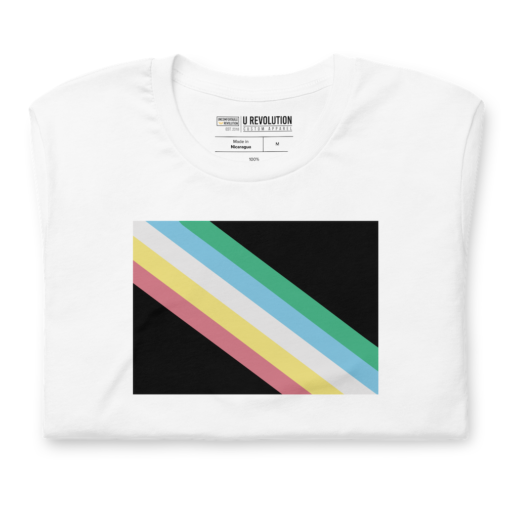 A folded white disability pride shirt. In the middle of the t-shirt is a dark grey-black background with five diagonal stripes in this order: red, yellow, white, blue, and green (when looking from the bottom up). The shirt is folded neatly with disability pride flag in the centre of the image.