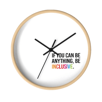 This diversity inclusion clock has a light wooden frame and a white background. The hands are black and there are no numbers. In the bottom white quadrant of the clock face is text printed in all caps: "IF YOU CAN BE ANYTHING, BE INCLUSIVE." All text in black, except "Inclusive," which is in rainbow colors.