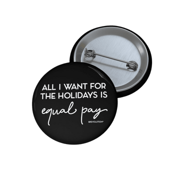 A photo of a round black equal pay pin button. In the middle of the equal pay pin phrase, 'All I want for the holidays is,' printed in large black upper case letters, with the words, 'equal pay,' printed directly beneath that phrase in black elegant cursive font. 