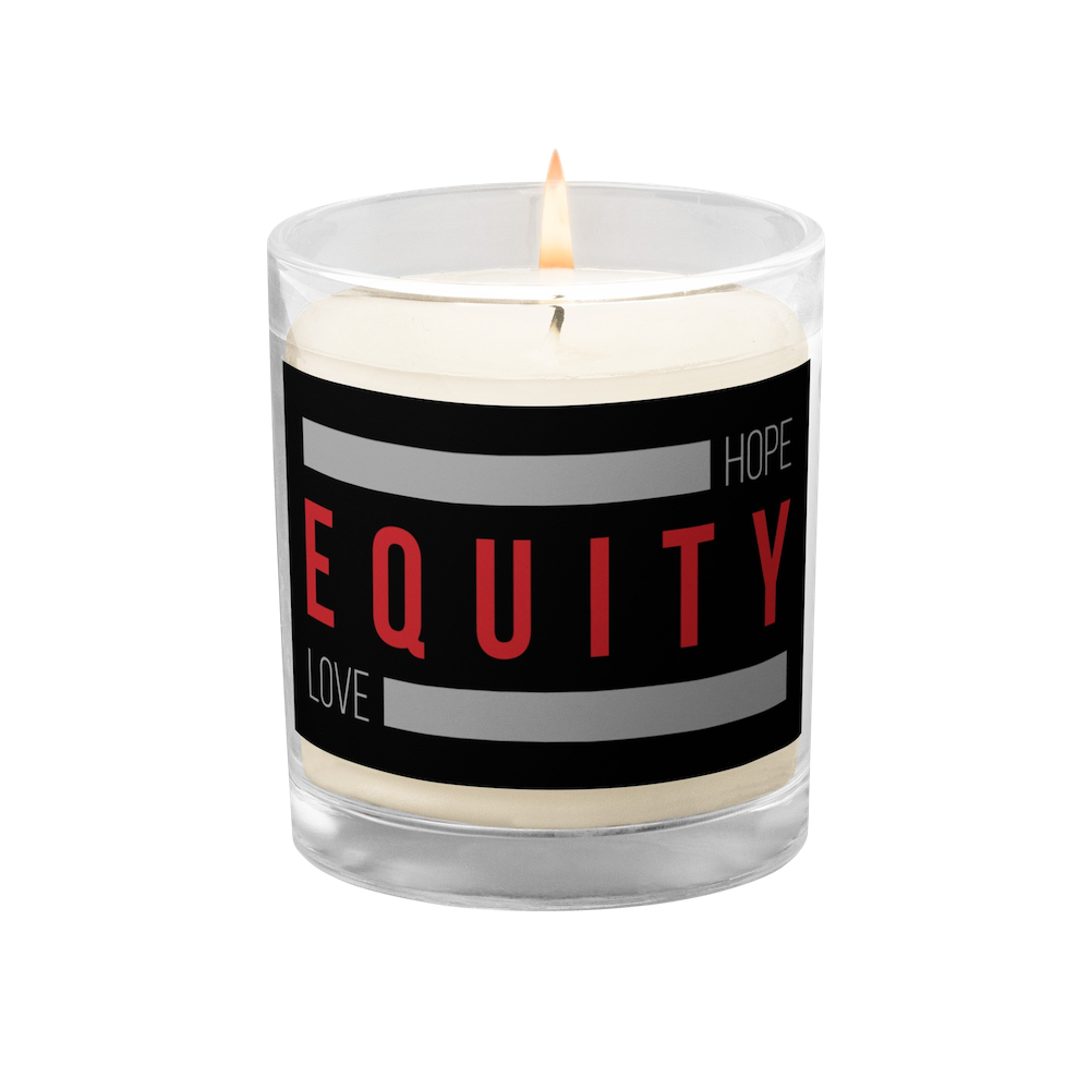 An Equity candle in a glass jar. On the outside of the jar is a black label. The word 'Equity' in upper case red letters is in the middle of the candle. Above and below the word are two thick rectangle blocks colored grey. The word HOPE is printed on the top right-hand side, and the word LOVE is on the bottom left side of the block. The candle's wick is lit.