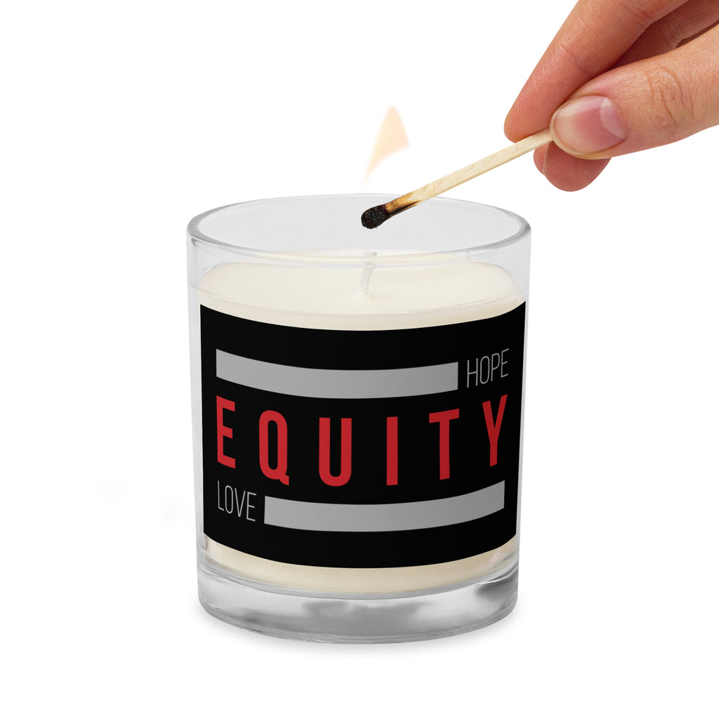 An Equity candle in a glass jar. On the outside of the jar is a black label. The word 'Equity' in upper case red letters is in the middle of the candle. Above and below the word are two thick rectangle blocks colored grey. The word HOPE is printed on the top right-hand side, and the word LOVE is on the bottom left side of the block. A match is lighting the wick.