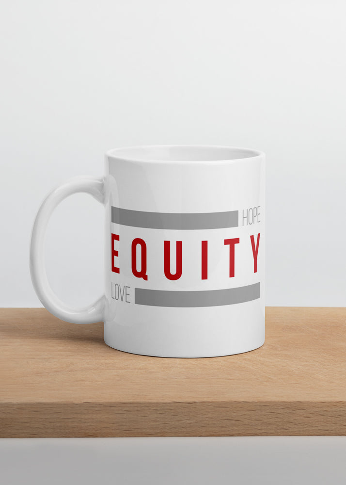 A 11 oz white ceramic Equity mug. In the middle of the mug is the word 'Equity' in upper case red letters. Above and below the word are two thick rectangle blocks colored grey. The word HOPE is printed on the top right-hand side, and the word LOVE is on the bottom left side of the block. The mug is displayed on a wooden cutting board.