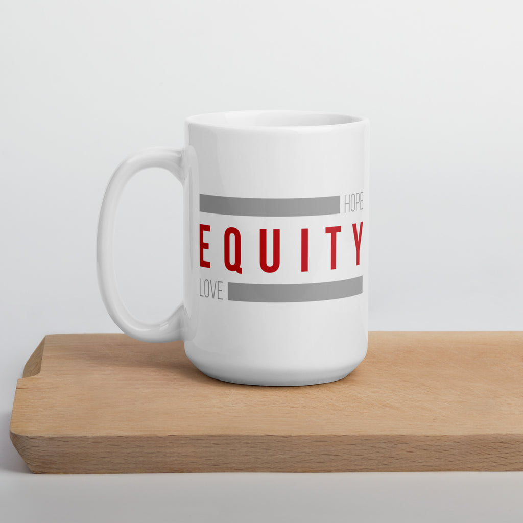 A 15 oz white ceramic Equity mug. In the middle of the mug is the word 'Equity' in upper case red letters. Above and below the word are two thick rectangle blocks colored grey. The word HOPE is printed on the top right-hand side, and the word LOVE is on the bottom left side of the block. The mug is displaced on a white cutting board.
