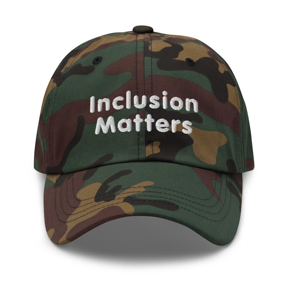 This is a photo of a green-camo Inclusion Matters Baseball Cap. On the front of the baseball cap above the visor are two words, 'Inclusion Matters.' printed in white sentence case letters over two lines.