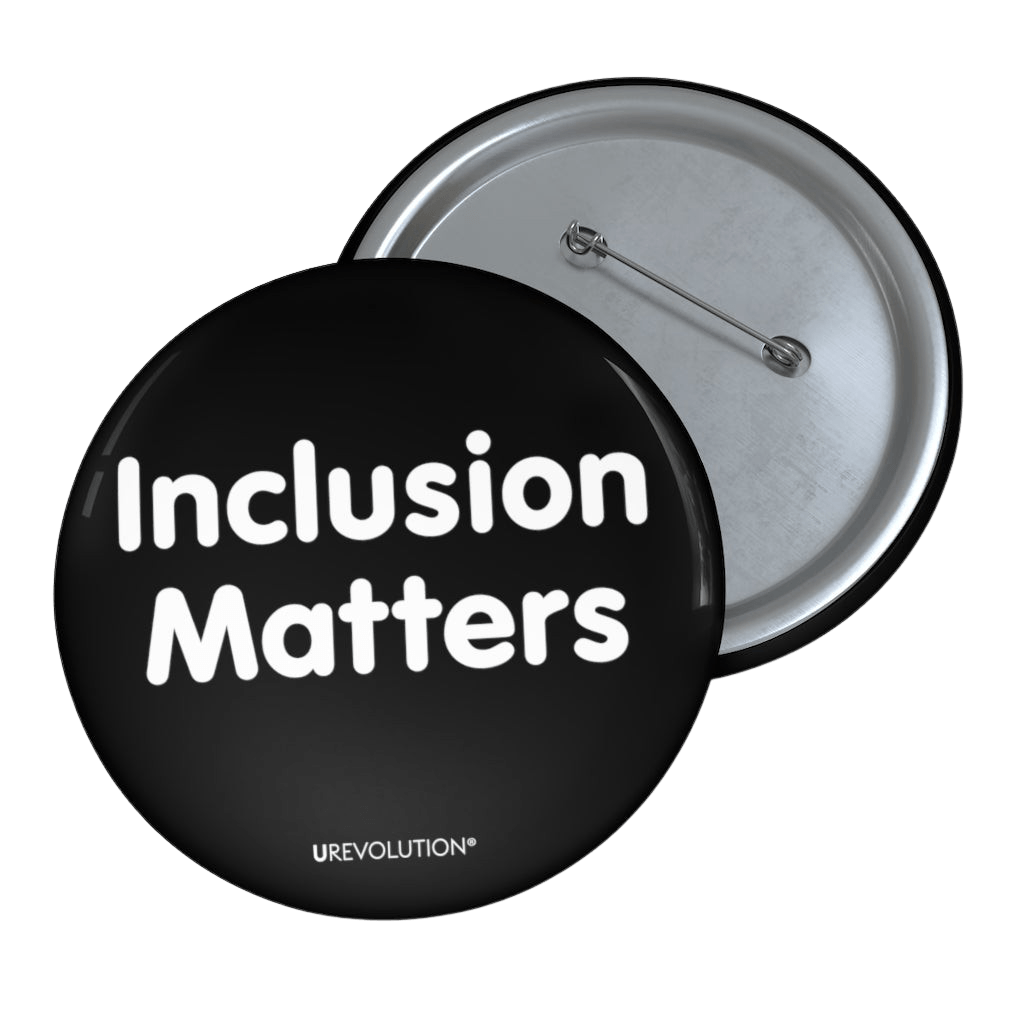 A black Inclusion Matters pin button against a plain white background. On the front of the pin button are two words, 'Inclusion Matters.' printed in white sentence case letters over two lines. At the bottom edge of the inclusion badge, beneath the phrase, 'Inclusion Matters,' is the brand name URevolution in small white upper case letters.