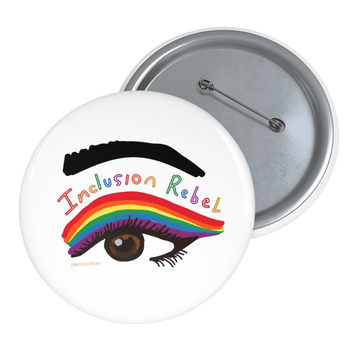 A photo of an inclusion rebel pin button. On the pin is an illustration of a giant brown eye with big black lashes and rainbow eye shadow. The words Inclusion Rebel are printed between the eye shadow and a thick black eyebrow in a handwritten font with a different rainbow color for each letter.
