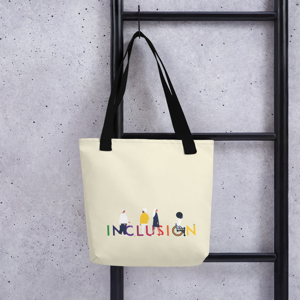 A disability inclusion tote bag has the word INCLUSION printed in rainbow-like colors on one side. The inclusion tote is canvas color with black straps. Four diverse disabled people have incorporated into the phrase INCLUSION: a blind person, a person with an invisible illness, a disabled person with a prosthetic limb, and a disabled person in a wheelchair.