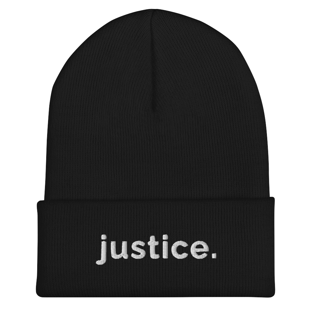 A black a justice beanie has the word 'justice.' embroidered in white lower case letters on the front of the beanie.