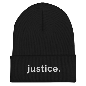 A black a justice beanie has the word 'justice.' embroidered in white lower case letters on the front of the beanie.