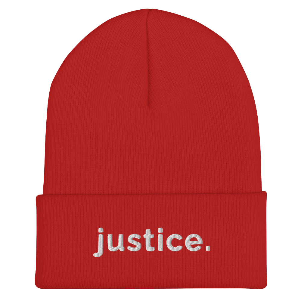 A red a justice beanie has the word 'justice.' embroidered in white lower case letters on the front of the beanie.