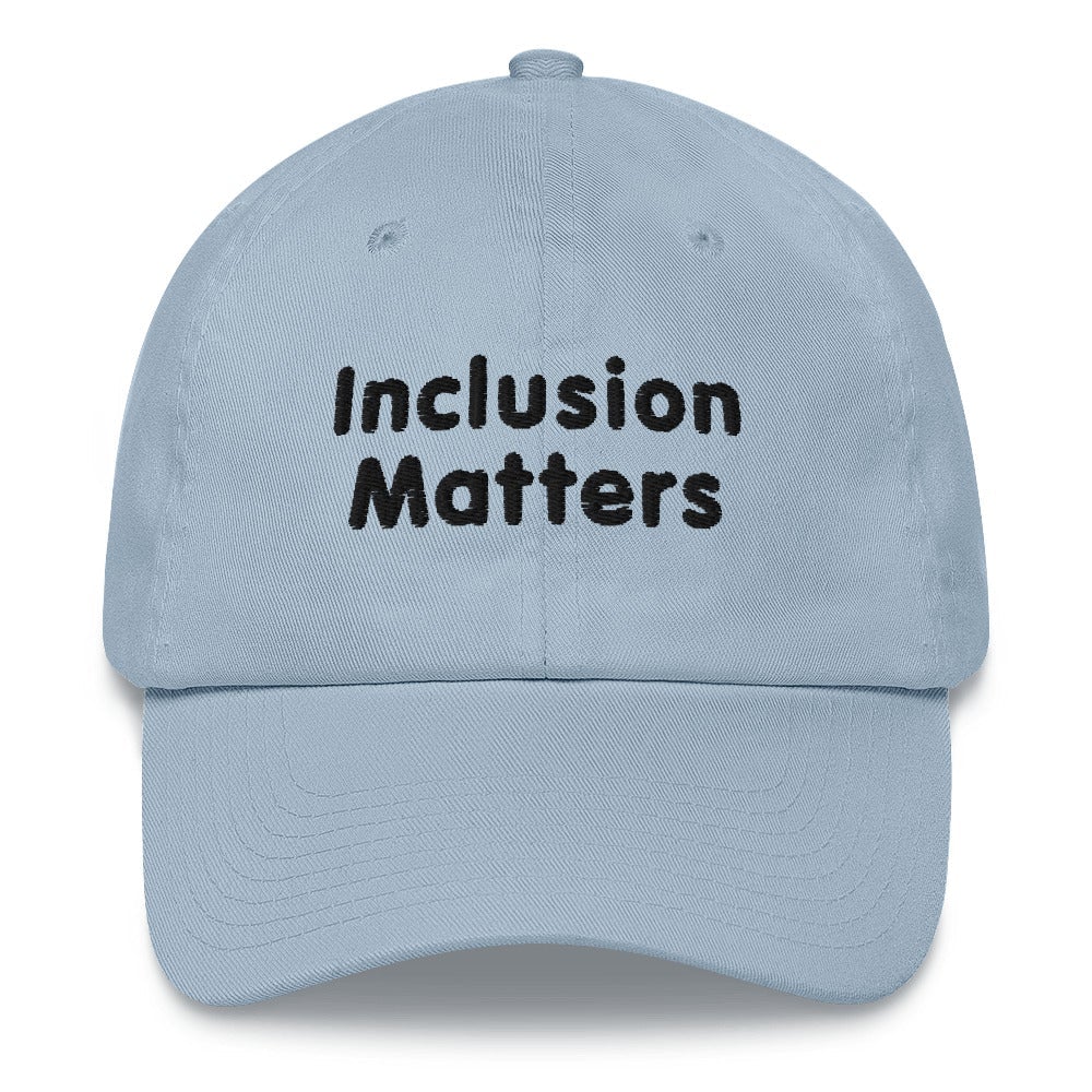 This is a photo of a light-blue Inclusion Matters Baseball Cap. On the front of the baseball cap above the visor are two words, 'Inclusion Matters.' printed in black sentence case letters over two lines.