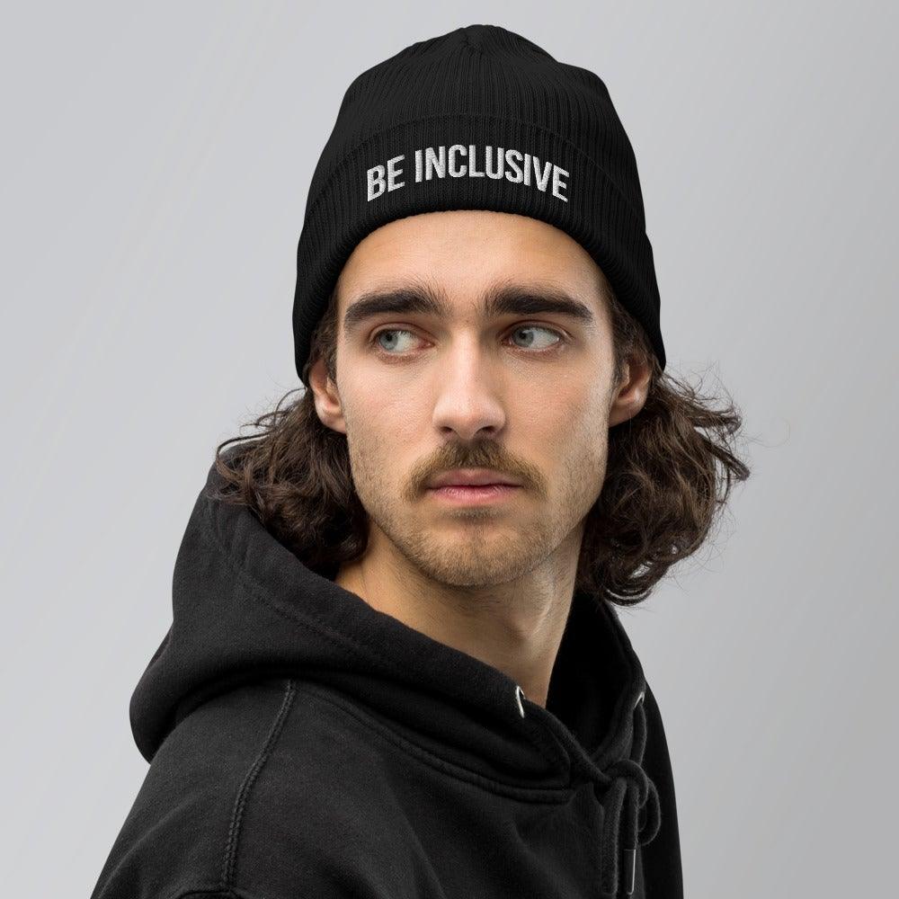This is a photo of a person with a beard standing against a white background wearing a black hoodie and a black Be Inclusive organic beanie. The words 'Be Inclusive' are embroidered on the front of the beanie in white upper case letters.