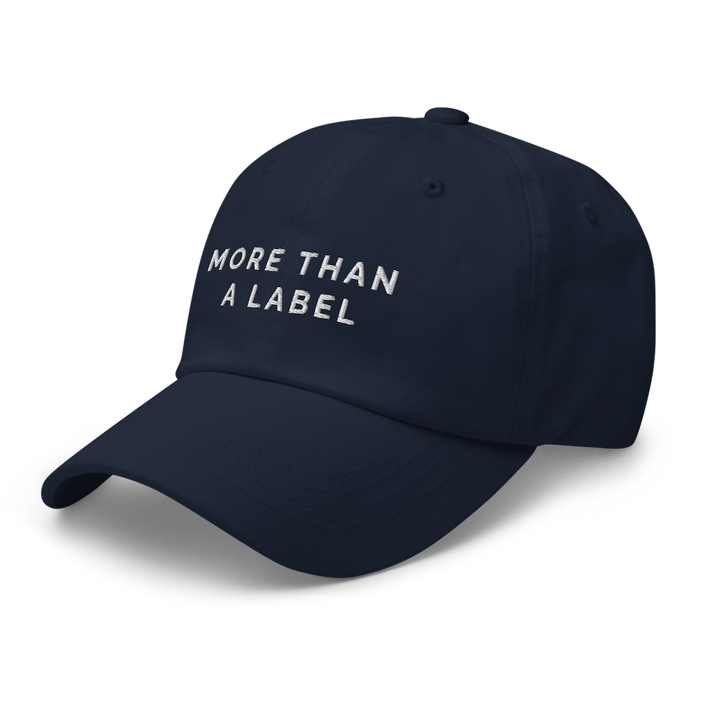 A side view of a navy More Than A Label cap. In the middle of the cap is the phrase, 'More Than A Label,' embroidered in white upper case letters.