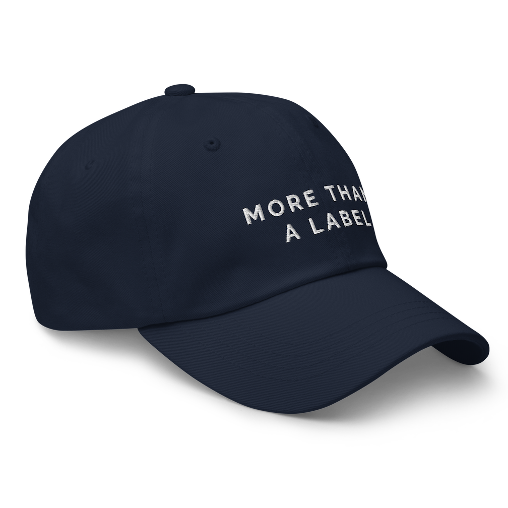 A side view of a navy More Than A Label cap. In the middle of the cap is the phrase, 'More Than A Label,' embroidered in white upper case letters.