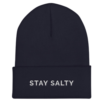 A photo of a navy hypoallergenic Stay Salty Beanie lying flat against a plain background. On the cuff of the beanie the phrase, 'Stay Salty,' is embroidered on it in white upper case letters. 