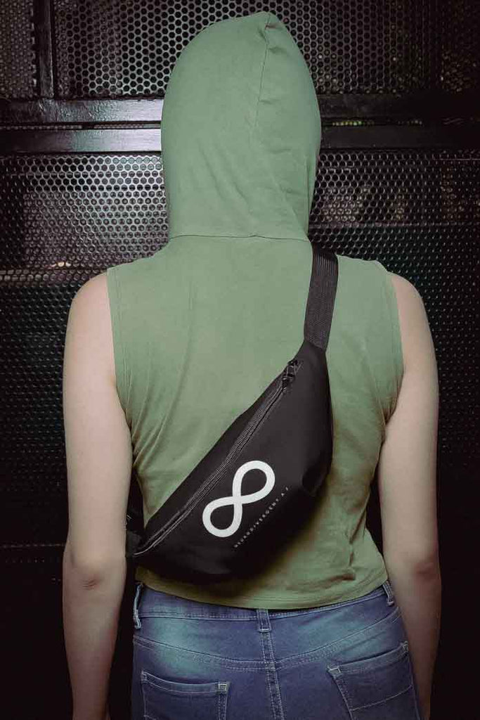 This is a photo of a black Neurodivergent AF waist bag. On the front of the waist bag is an thick white infinity symbol consisting. Just below the symbol is the word 'Neurodivergent AF' in elegant upper case white letters. The waist pack is worn on the back of a model wearing a short-sleeve green hoodie