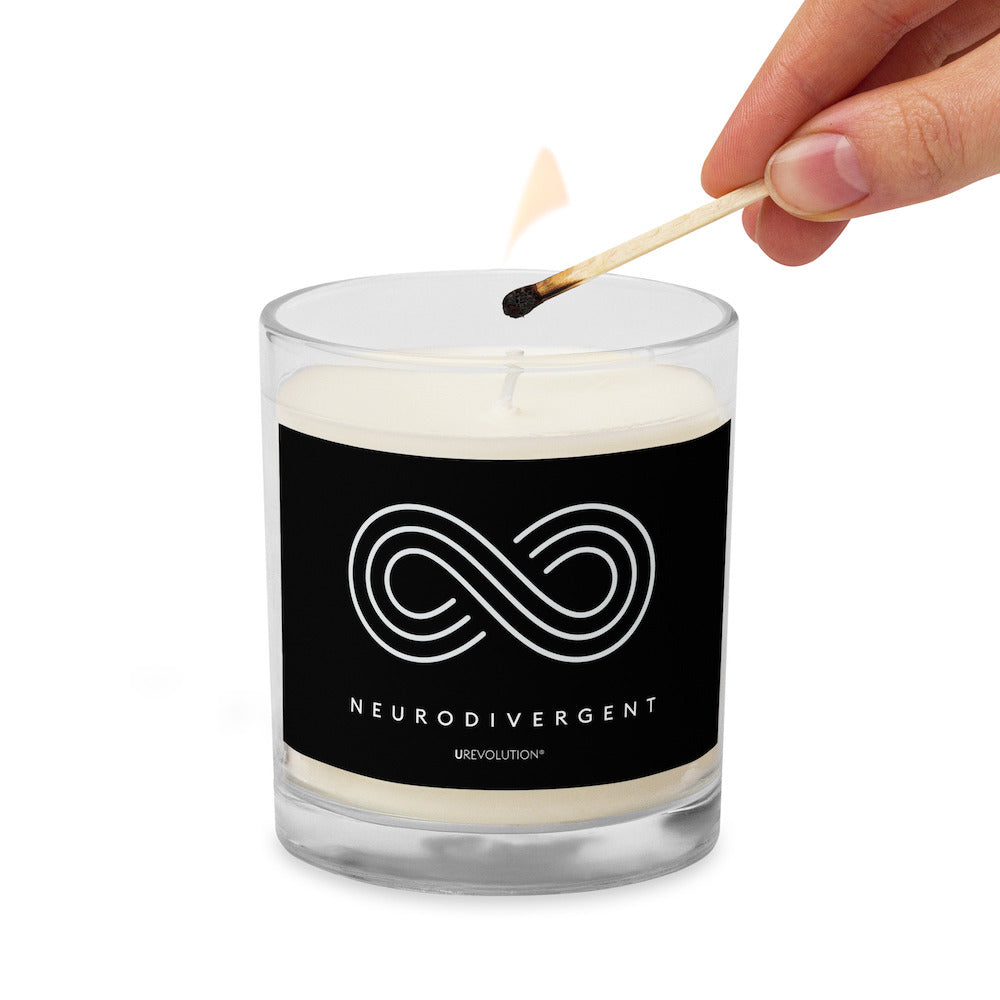 Neurodivergent candle by URevolution. This is a photo of a candle in a glass jar with a black label. In the middle of the black label is a three-ringed infinity symbol with the word 'neurodivergent' in white upper case letters beneath the symbol.  The candle is being lit by a match.