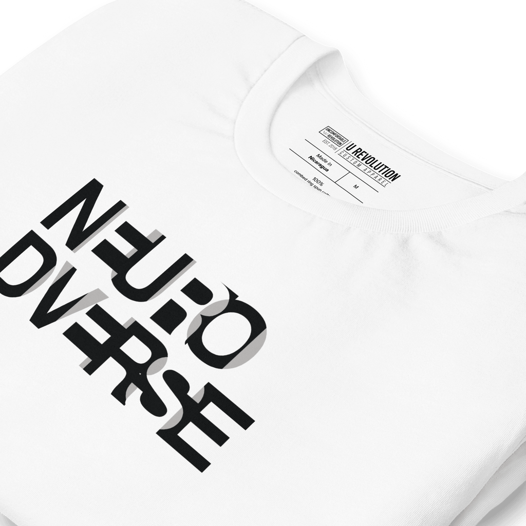 This is a close-up photo of a white NeuroDiverse t-shirt that has the text NEURODIVERSE printed in large alternating black and white letters on the front, taking up about one-third of the shirt surface.  