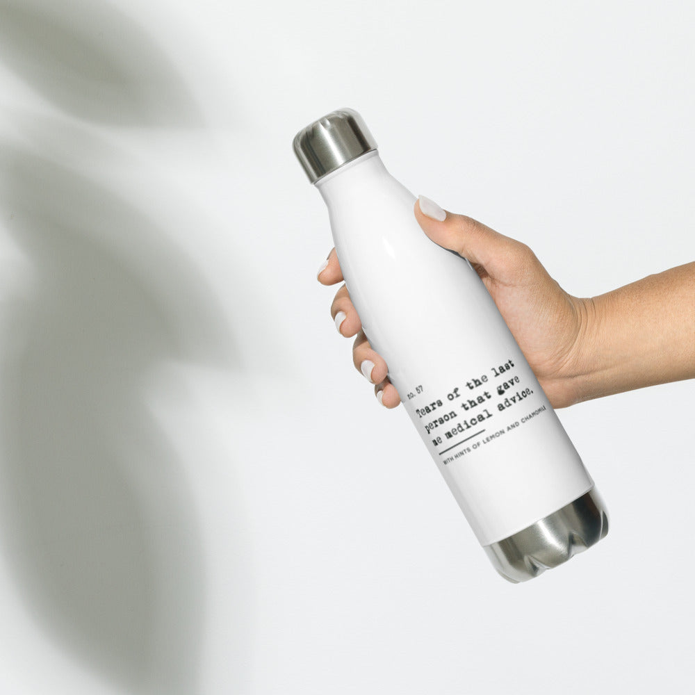 The no medical advice water bottle is white, shaped like a bowling pib, with black text that reads: "no. 57. Tears of the last person that gave me medical advice. With hints of lemon and chamomile." The bottle is shaped like a bowling pin. The water bottle is being held in a person's hand.
