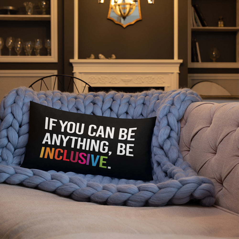 This is an image of a black premium Be Inclusive throw cushion. In the middle of the rectangle throw cushion, the following phrase is printed in white upper case letters, "IF YOU CAN BE ANYTHING, BE INCLUSIVE." The word INCLUSIVE is in rainbow-like colors. 