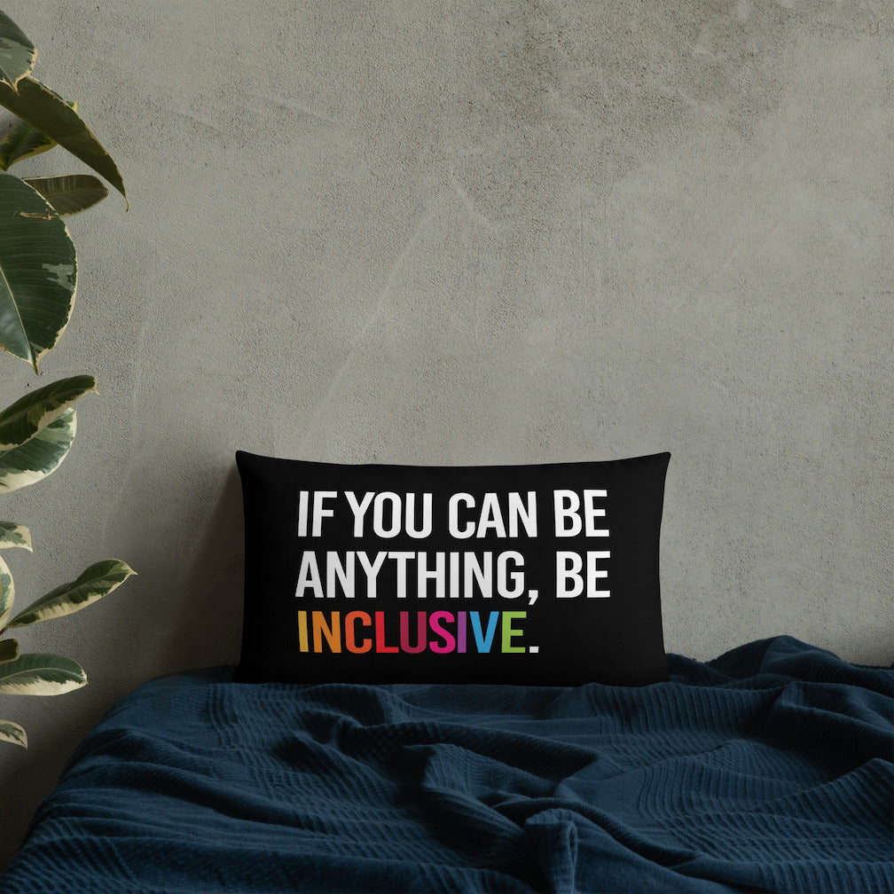 This is an image of a black premium Be Inclusive throw cushion. In the middle of the rectangle throw cushion, the following phrase is printed in white upper case letters, "IF YOU CAN BE ANYTHING, BE INCLUSIVE." The word INCLUSIVE is in rainbow-like colors. 