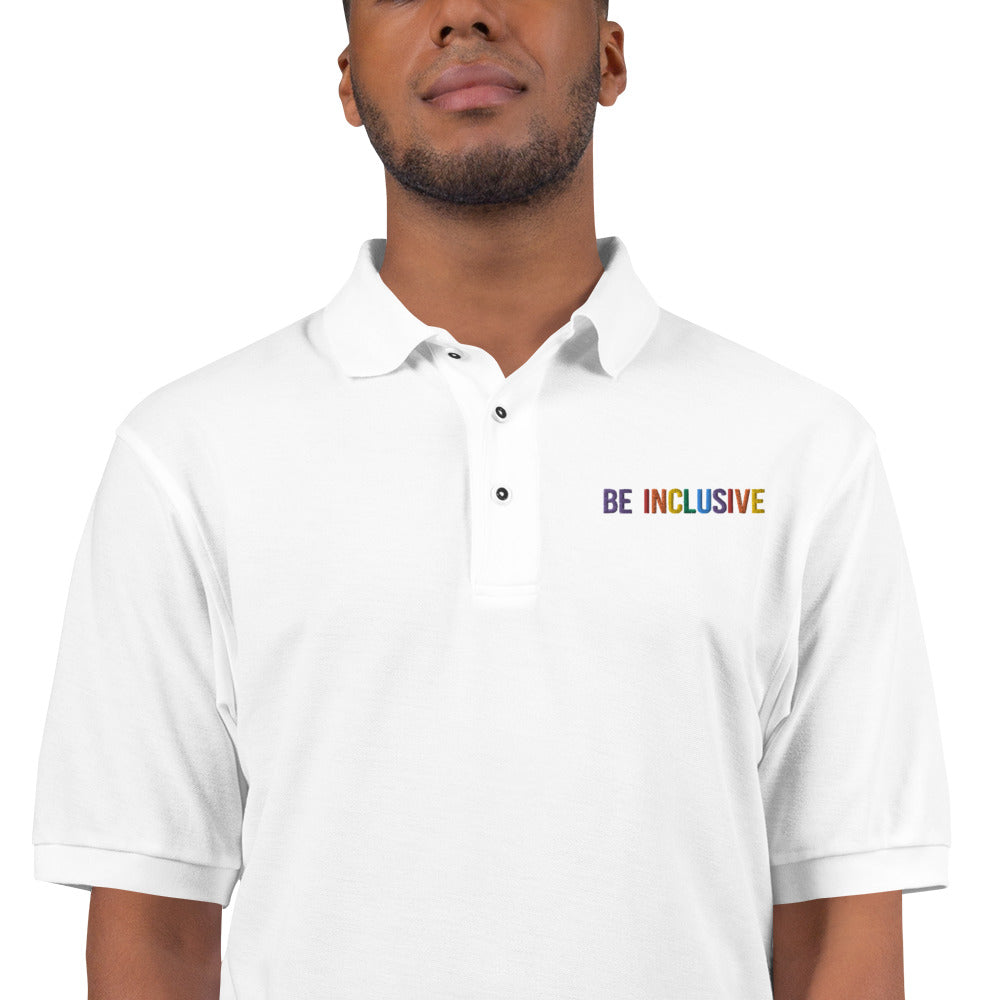 Photo of a premium white Rainbow Be Inclusive Polo Shirt. On the polo's top right panel is the phrase, Be Inclusive, embroidered in red, orange, yellow, green, indigo, and violet. The word 'be' is only in violet.