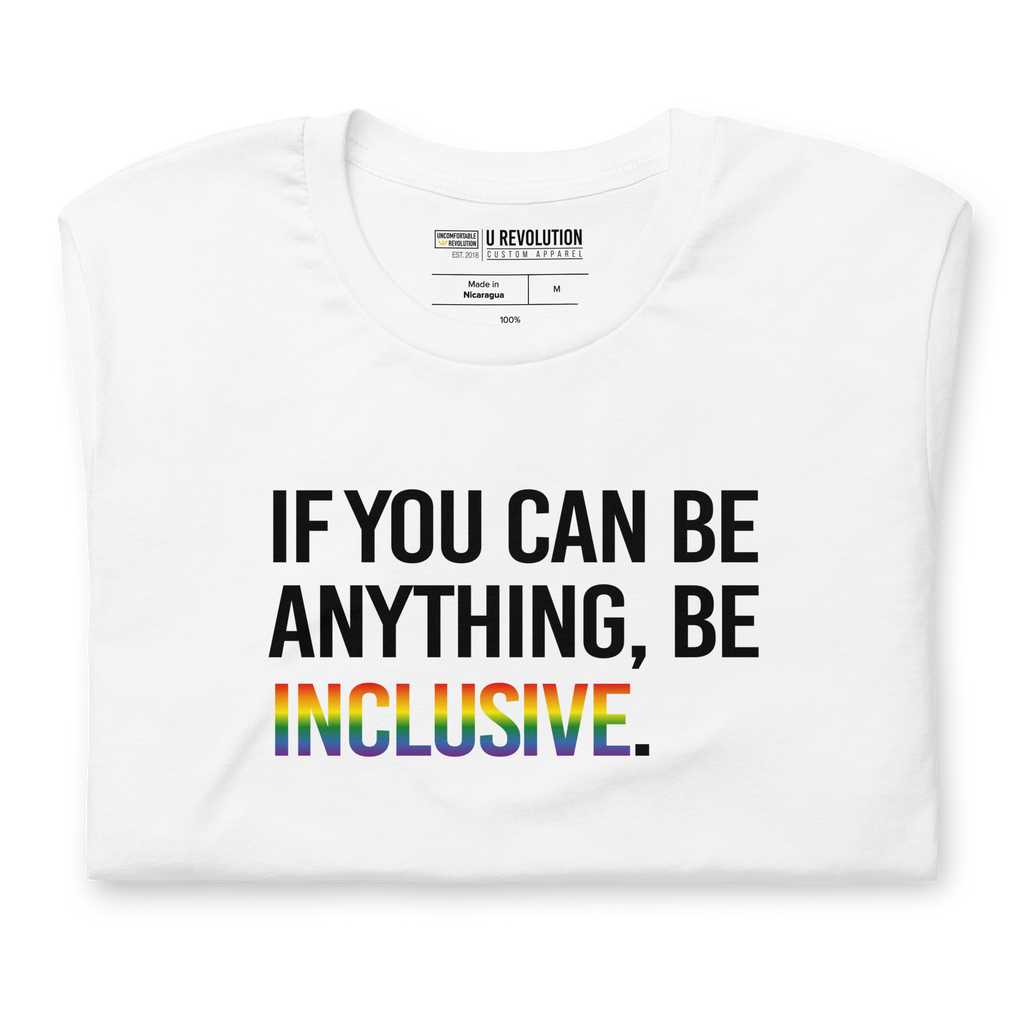 This is a photo of a white Rainbow Be Inclusive Pride Tee. On the front of the inclusive t-shirt is the phrase: "If you can be anything, be inclusive," in black upper case letters. All the text is in black, except "Inclusive," which is in blended upper case rainbow pride colors:  red, orange, yellow, green, indigo, and violet. The tee is folded showing the design only.