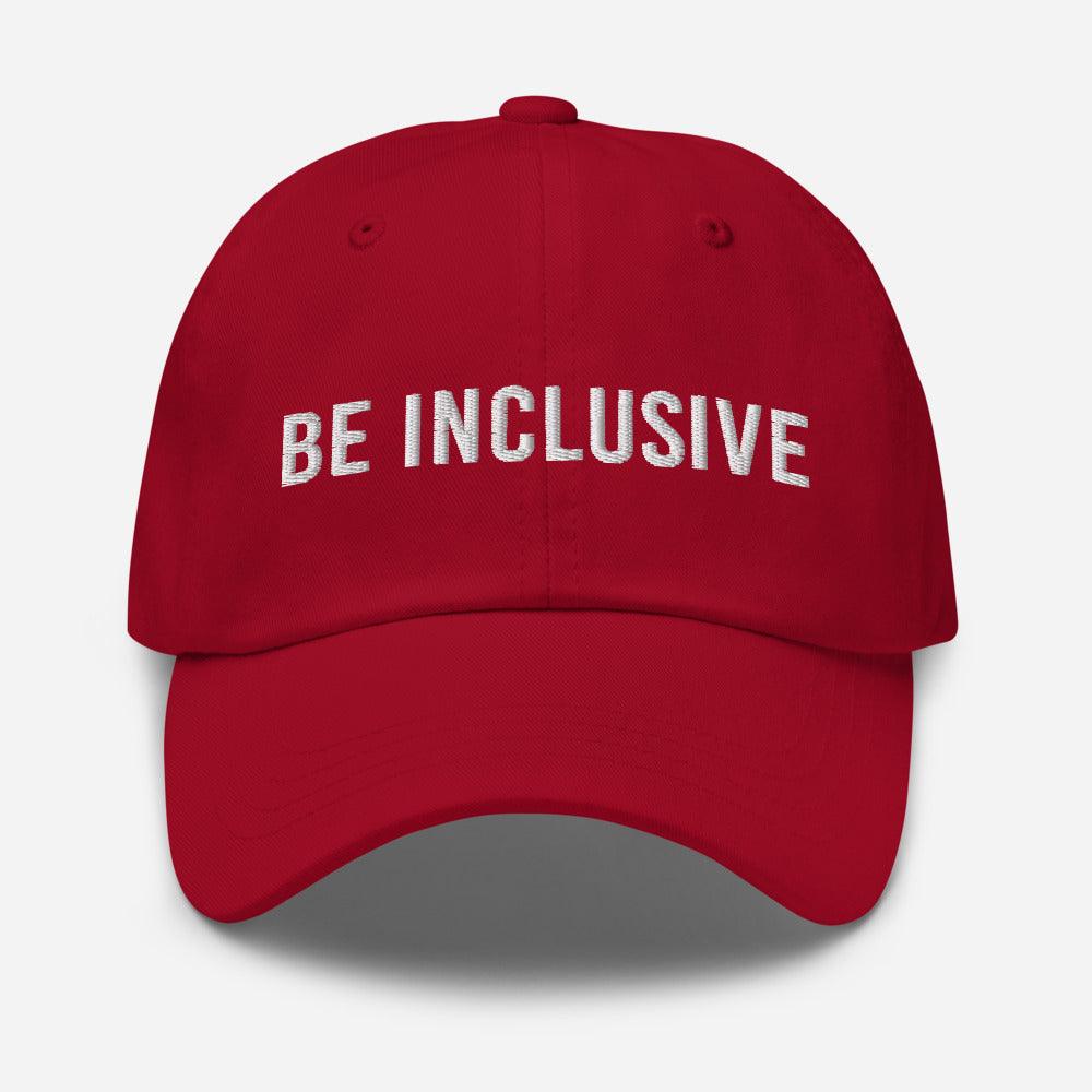 This is a photo of the front of a red cotton twill 'be inclusive cap,' with the phrase "Be Inclusive" embroidered on the front in upper case white letters.