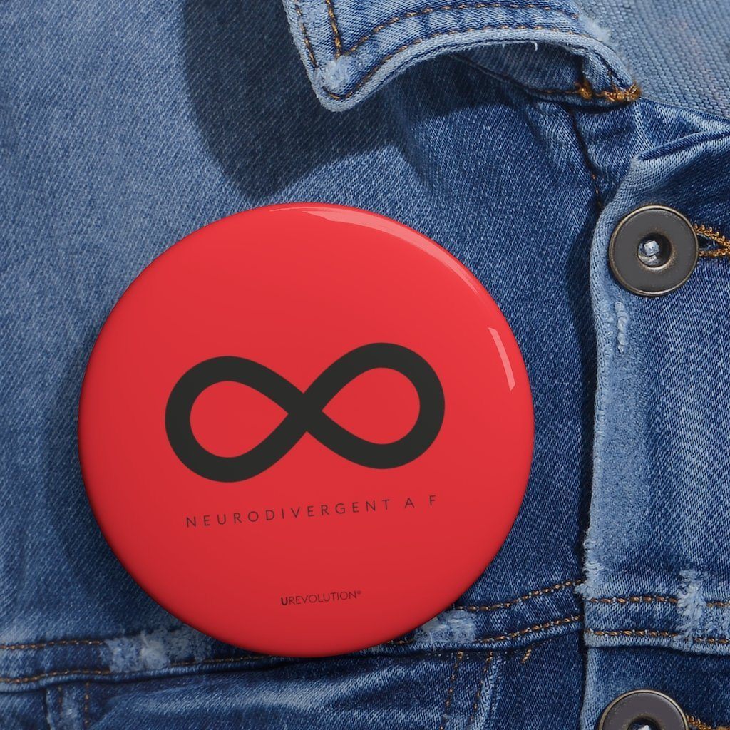 A photo of URevolution's round  neurodivergent pin badge. The neurodivergent pin is red and features a black infinity symbol, the symbol of the neurodiversity movement. Under the symbol is the phrase, 'neurodivergent a__f.'