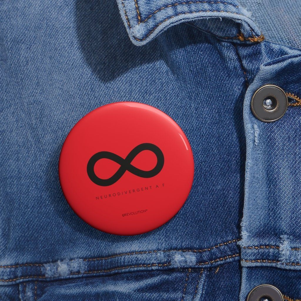 A photo of URevolution's round  neurodivergent pin badge. The neurodivergent pin is red and features a black infinity symbol, the symbol of the neurodiversity movement. Under the symbol is the phrase, 'neurodivergent a__f.'