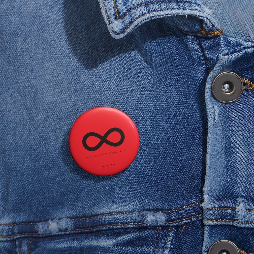 A photo of URevolution's round  neurodivergent pin badge. The neurodivergent pin is red and features a black infinity symbol, the symbol of the neurodiversity movement. Under the symbol is the phrase, 'neurodivergent a__f.'