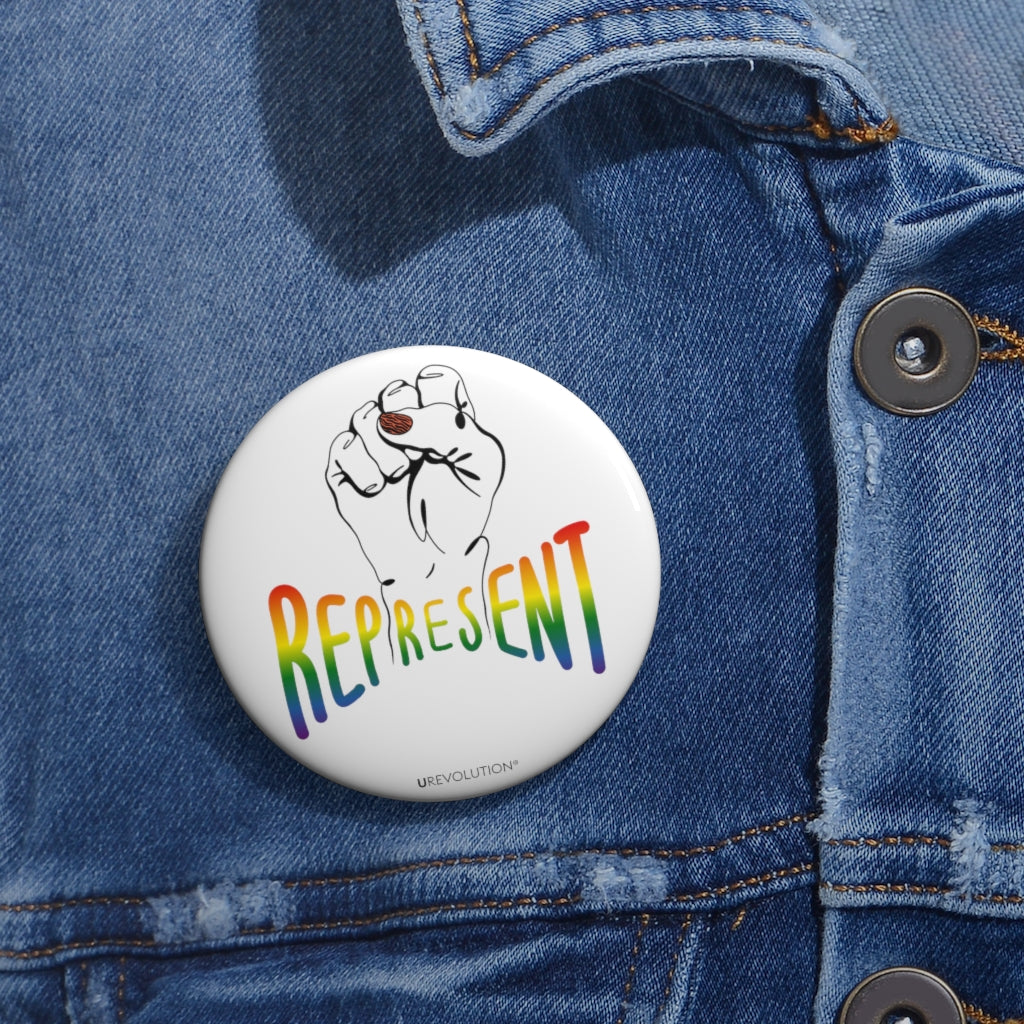 Represent Pride Pin Button. In the middle of the represent pride pinback button is a black line drawing of a raised clenched fist, with the handwritten word "represent," written in blended upper case rainbow pride colors: red, orange, yellow, green, indigo, and violet. Under the fist, at the bottom of the magnet, is the word URevolution in small black upper case letters.. The 2.25 inch pin is displayed on the front of a faded blue denim jacket.