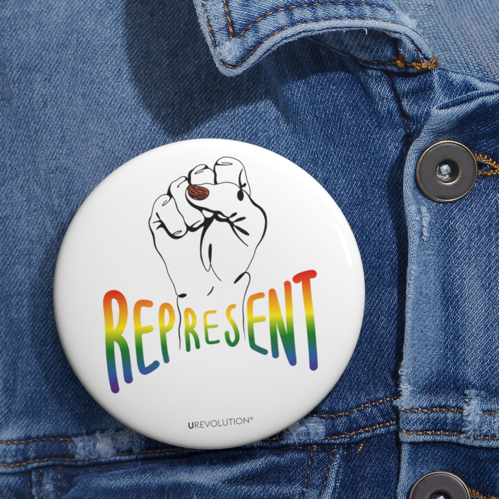 Represent Pride Pin Button. In the middle of the represent pride pinback button is a black line drawing of a raised clenched fist, with the handwritten word "represent," written in blended upper case rainbow pride colors: red, orange, yellow, green, indigo, and violet. Under the fist, at the bottom of the magnet, is the word URevolution in small black upper case letters.. The 3 inch pin is displayed on the front of a faded blue denim jacket.