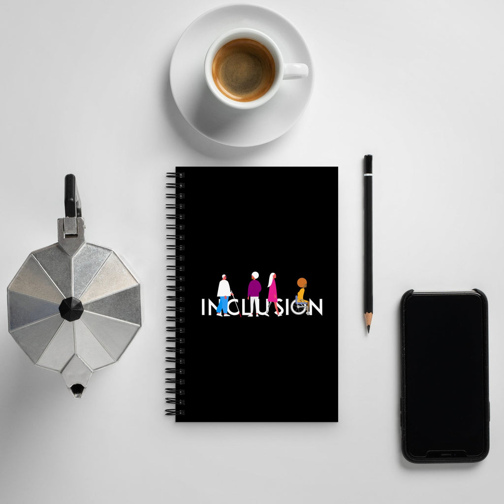 Inclusion Notebook. URevolution Inclusion Notebook features our unique Inclusion design, with the word INCLUSION in upper case in rainbow colors. INCLUSION word has figures of different disabled people interspersed among the INCLUSION letters. The notebook is on a coffee table.