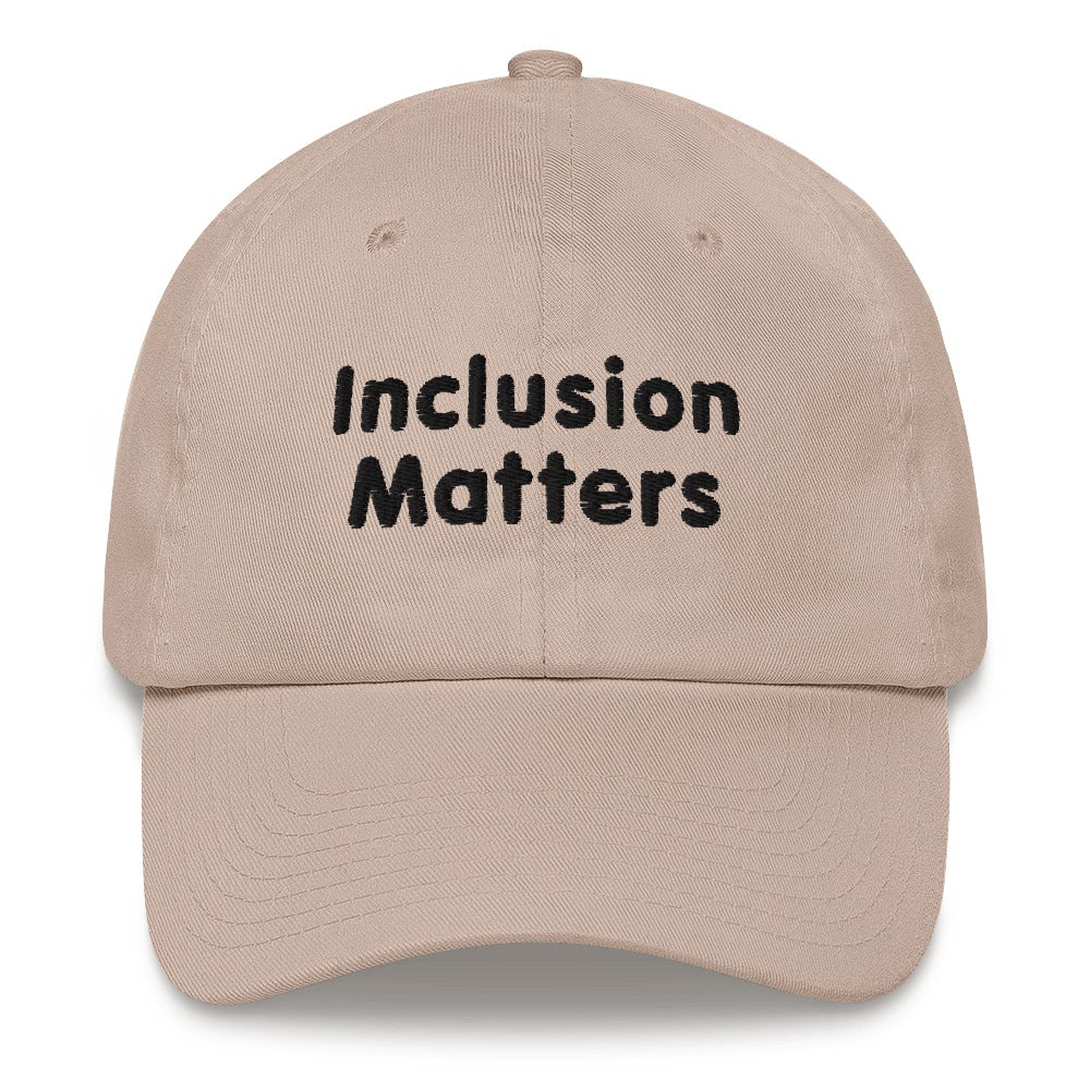 This is a photo of a stone Inclusion Matters Baseball Cap. On the front of the baseball cap above the visor are two words, 'Inclusion Matters.' printed in black sentence case letters over two lines.